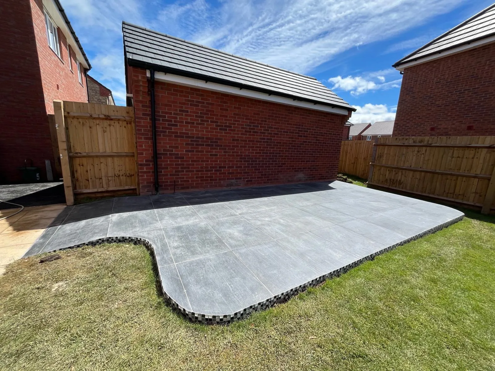 Newly laid grey porcelain patio with curved border