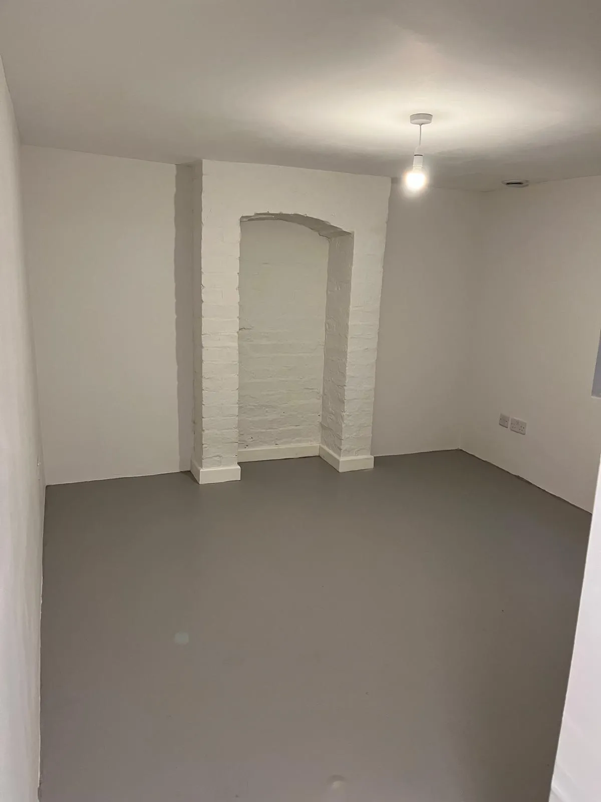 Freshly redecorated basement room with painted brick alcove and grey floor