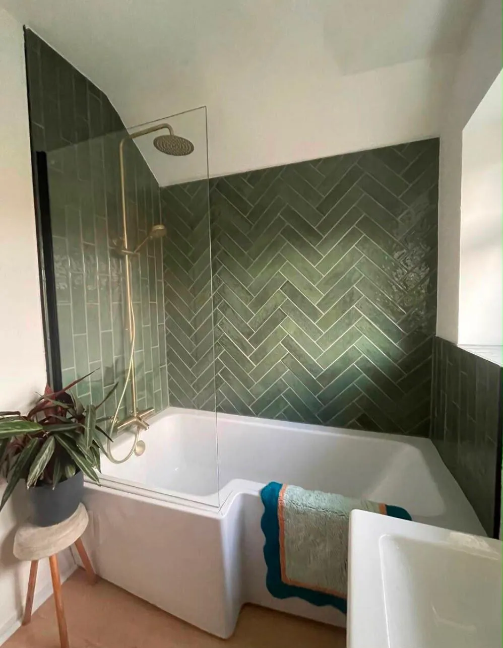 Refurbished bathroom with green herringbone tiles and brushed brass shower