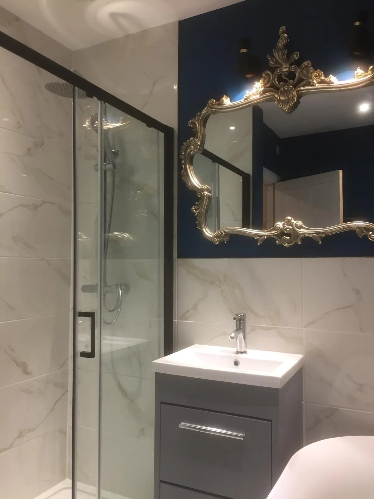Newly fitted shower room with marble-effect tiling, grey vanity unit and ornate gold mirror