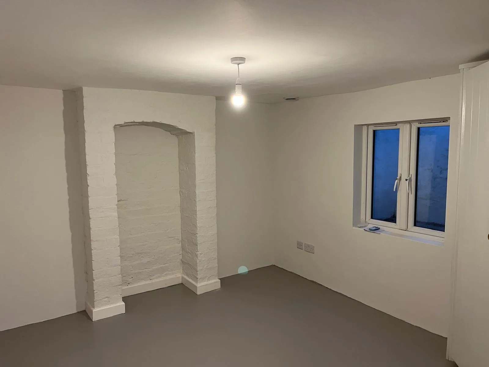Freshly decorated empty room with whitewashed brick alcove and grey floor