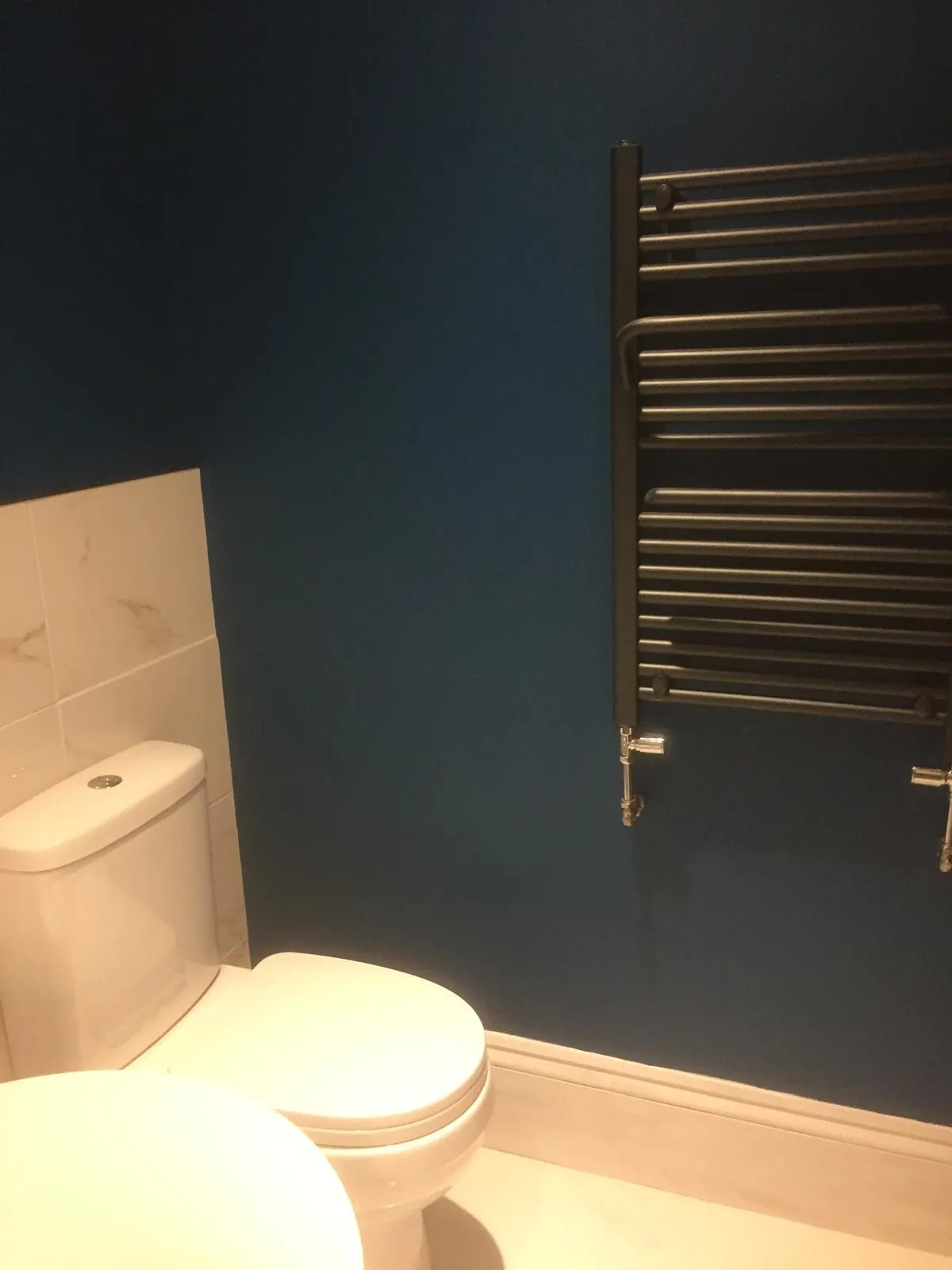 Finished bathroom with navy walls, marble-effect tiling and anthracite towel rail
