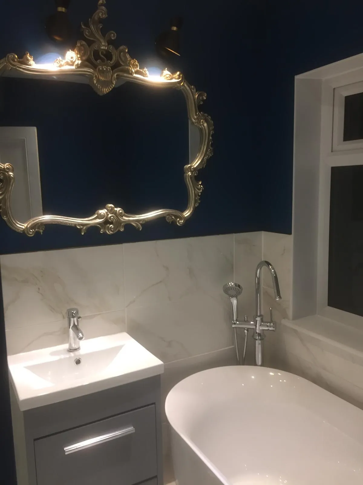 Refurbished bathroom with navy walls, marble-effect tiles and freestanding bath